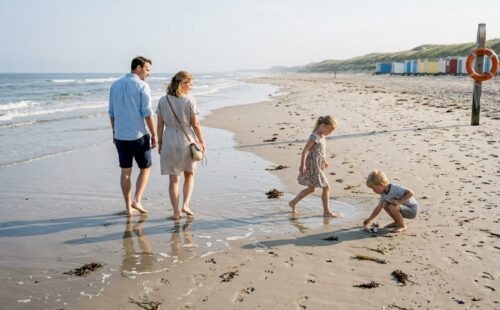 Een gezin wandelt samen over het uitgestrekte, rustige strand.