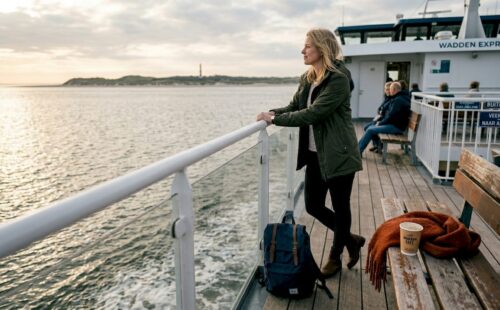 Een vrouw geniet van het uitzicht op de veerboot die richting een Waddeneiland vaart.