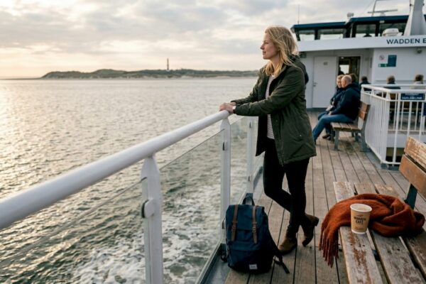 Een vrouw geniet van het uitzicht op de veerboot die richting een Waddeneiland vaart.