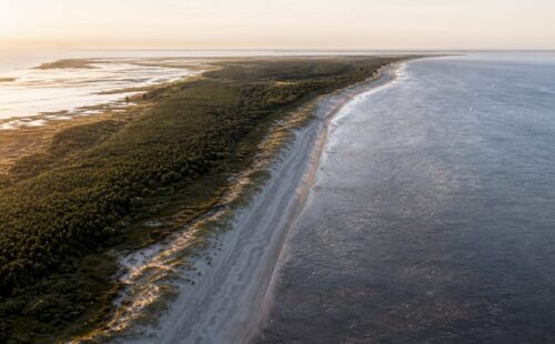 Een prachtige luchtfoto van Ameland, waarop de uitgestrekte kustlijn en het unieke landschap van het eiland goed zichtbaar zijn.