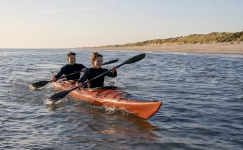 Een stel peddelt samen in een open kajak langs het strand van Ameland.