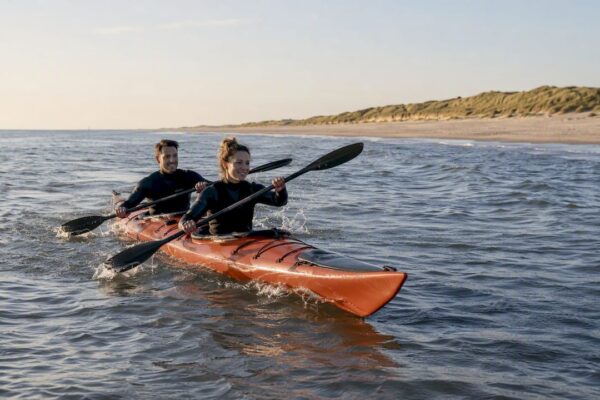 Een stel peddelt samen in een open kajak langs het strand van Ameland.