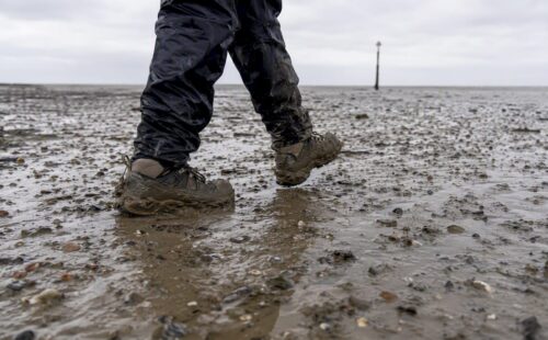 Voeten in stevige wandelschoenen op het wad, midden in het slik.