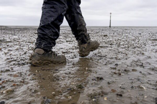 Voeten in stevige wandelschoenen op het wad, midden in het slik.