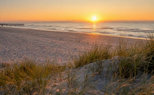 Een uitgestrekt, verlaten zandstrand verscholen achter de duinen van Ameland.