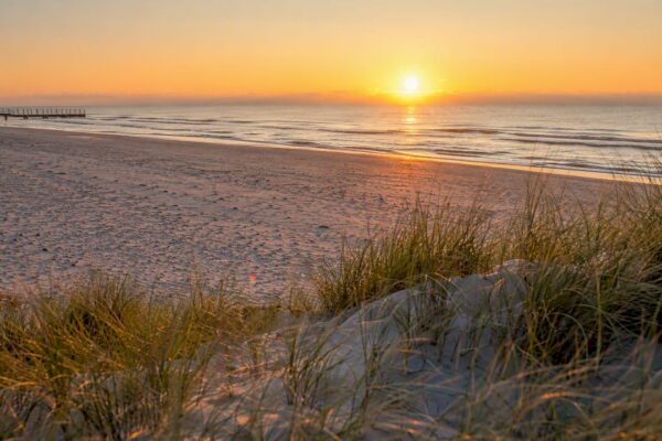 Een uitgestrekt, verlaten zandstrand verscholen achter de duinen van Ameland.