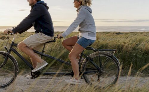 Een stelletje fietst samen op een tandem langs de duinen van Ameland.