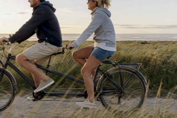 Een stelletje fietst samen op een tandem langs de duinen van Ameland.