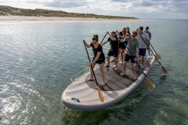 Een groep volwassenen peddelt samen op een mega-sup
